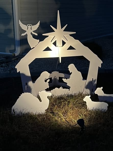 A decorative nativity scene featuring silhouettes of Mary, Joseph, baby Jesus, animals, and an angel, illuminated at night.