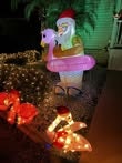 A festive decoration featuring an inflatable Santa with a pink flamingo float, surrounded by holiday lights and decorations.
