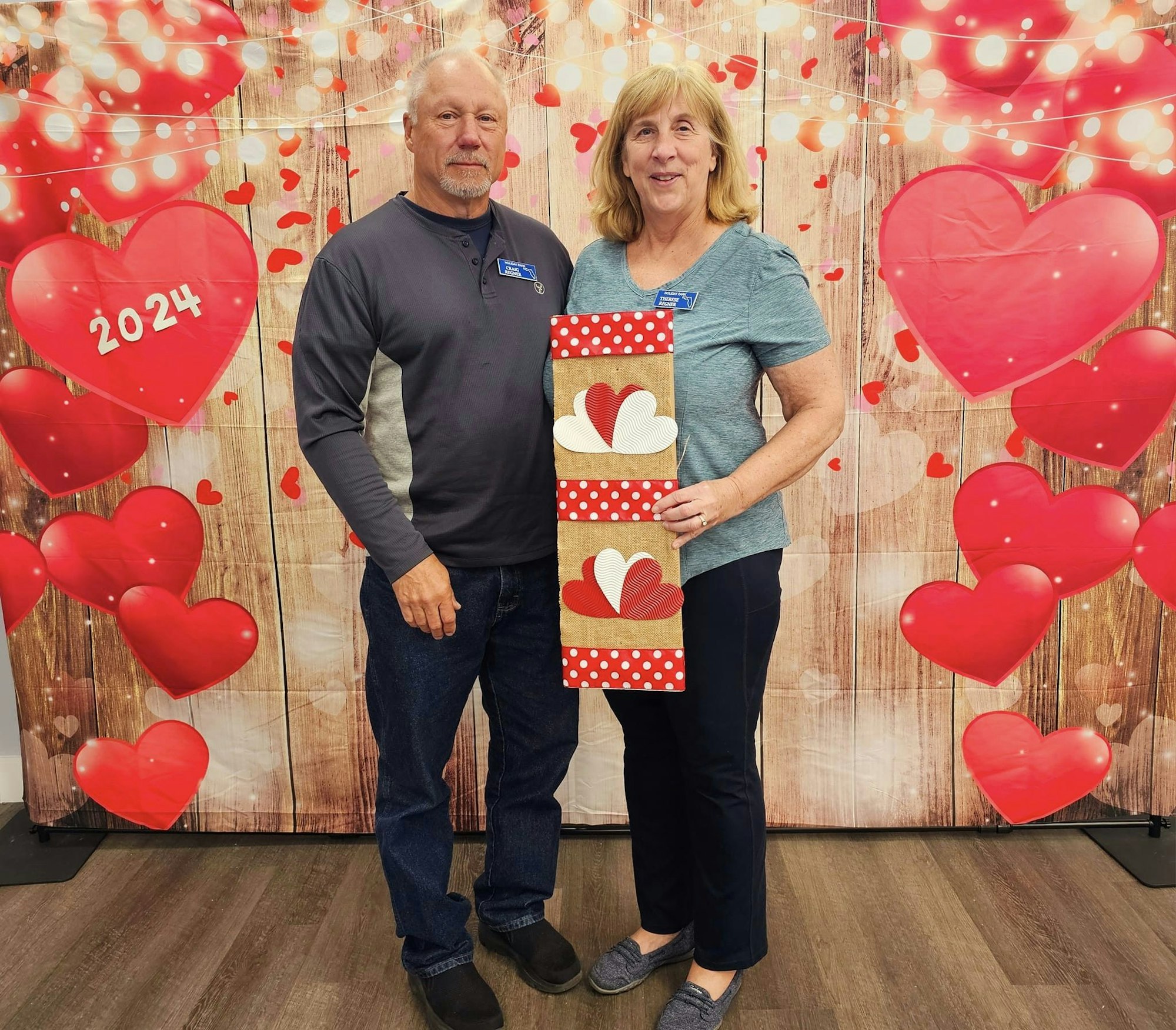 Two people posing with a Valentine's Day backdrop, red hearts, and decorations.