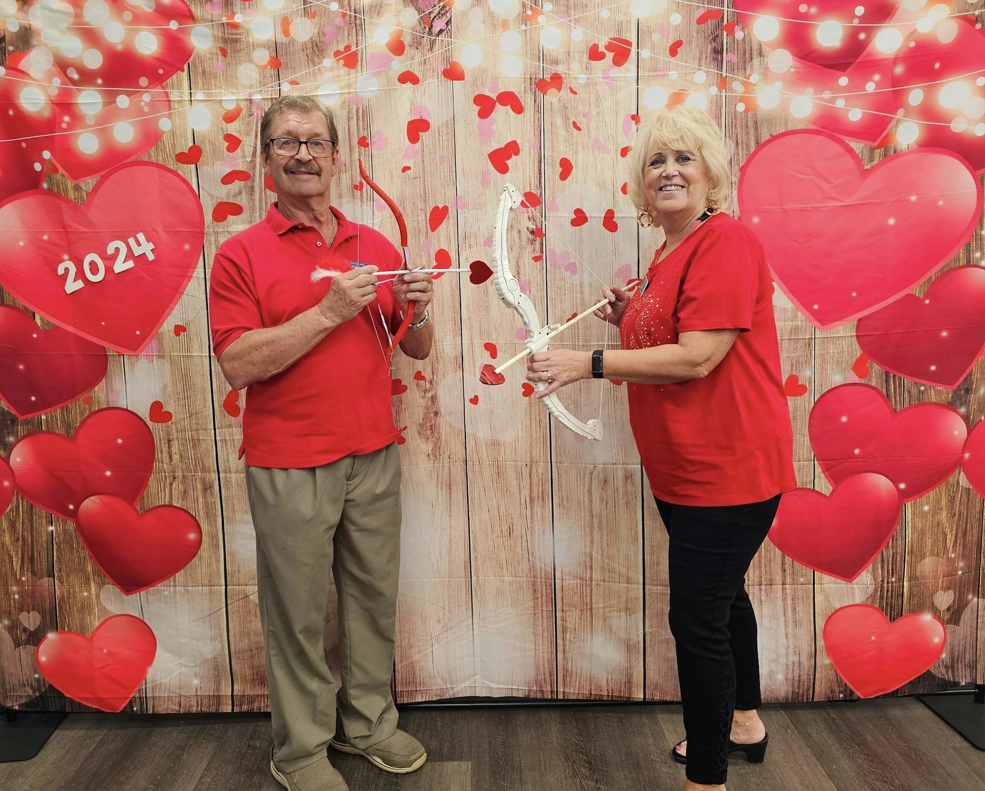 Two people with Cupid's bow and arrow amidst heart-themed Valentine's decor.