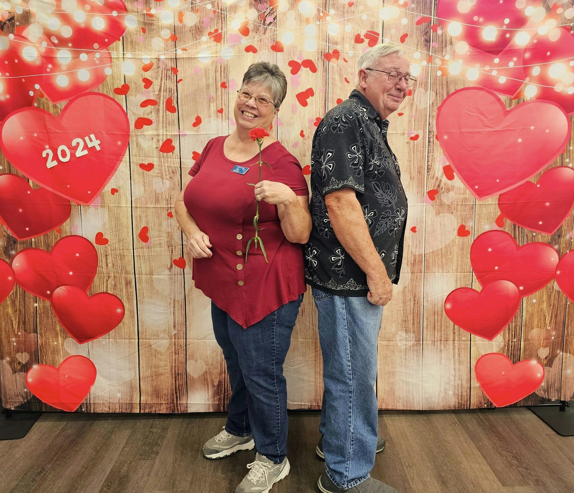 Two people smiling with a backdrop of hearts, possibly celebrating love or Valentine's Day.
