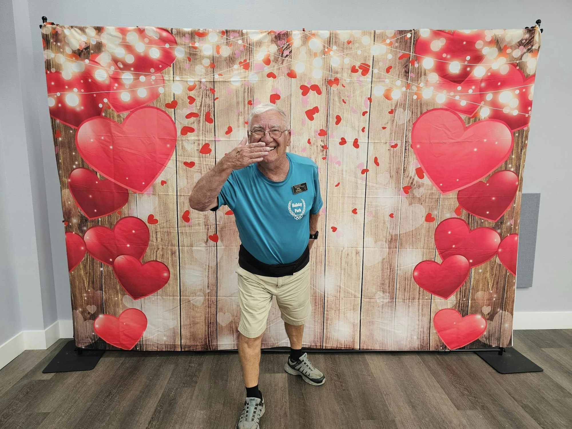 Smiling man with a playful gesture in front of a heart-decorated backdrop.