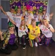 A lively group of people celebrating Mardi Gras, wearing festive outfits and accessories, with a colorful backdrop.