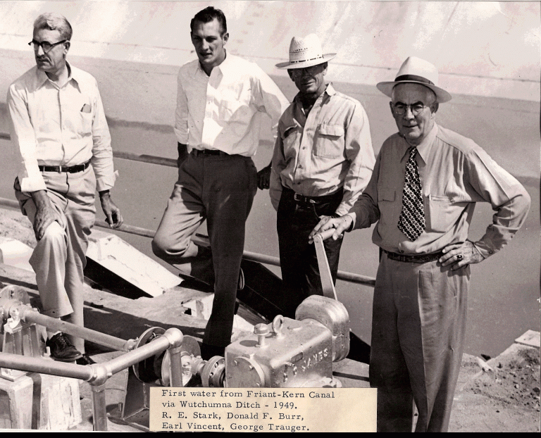 Four men standing near a canal, one in a hat. Text: "First water from Friant-Kern Canal via Wutchumna Ditch - 1949."