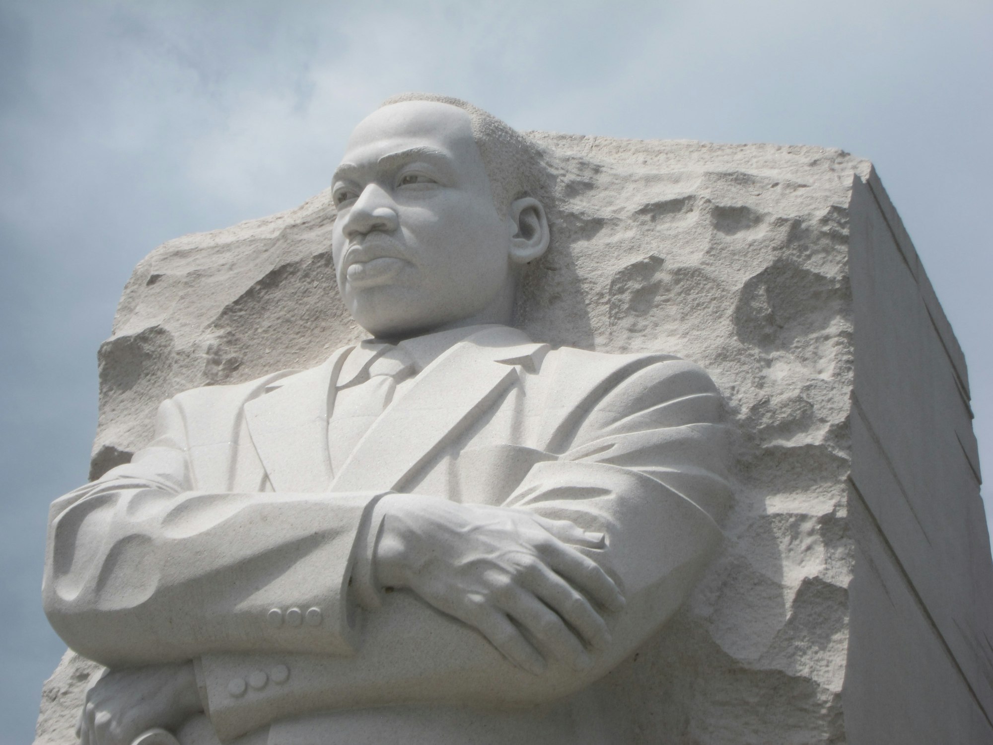 The image shows a stone monument of a prominent figure with crossed arms, symbolizing strength and leadership.