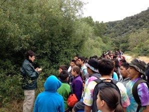A group of people, possibly on an outdoor educational trip, listening to a person who seems to be giving a talk or instruction.