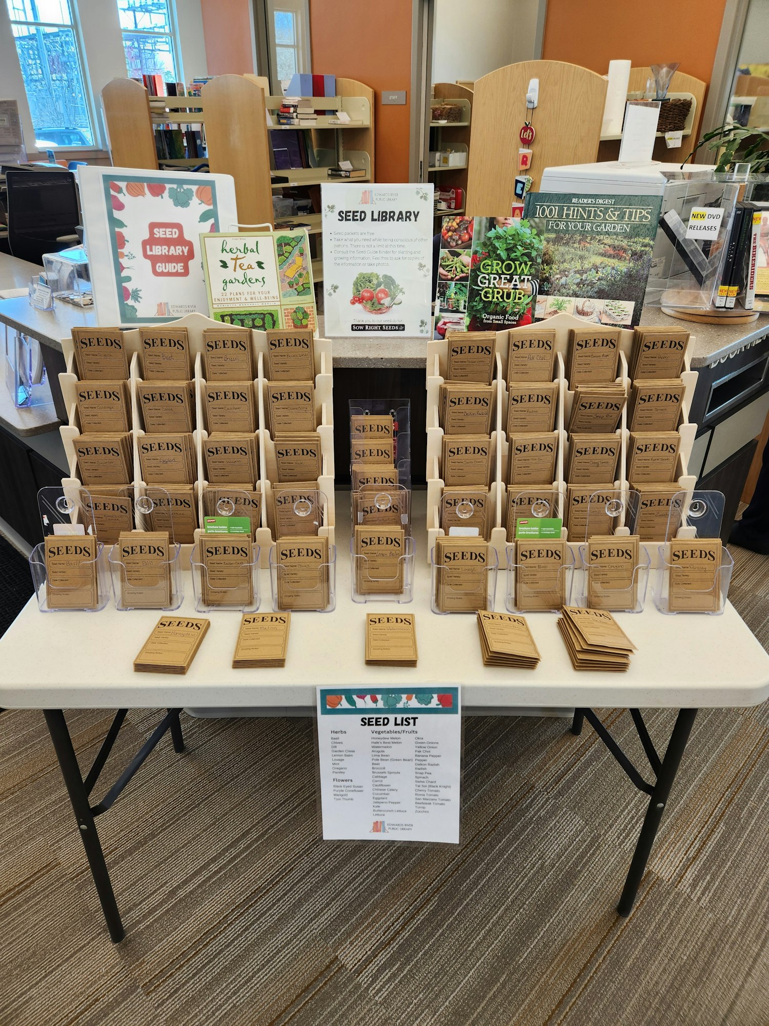 A table with seed packets, books, and a "Seed Library" sign, offering gardening resources and a seed list.