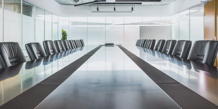 A modern conference room with a long table and black chairs, featuring large windows and a projector in the center.