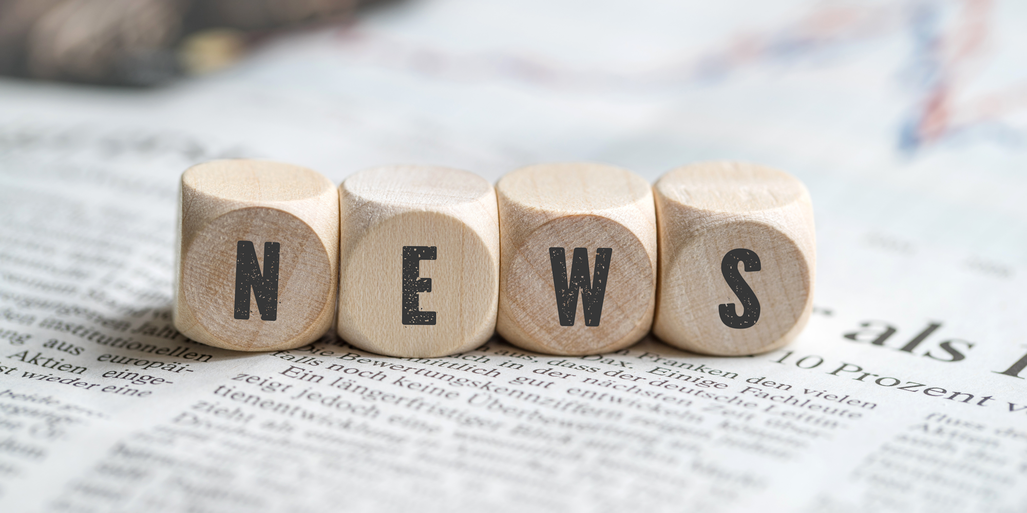 The image features wooden blocks spelling "NEWS" on a newspaper background, emphasizing the theme of information and reporting.