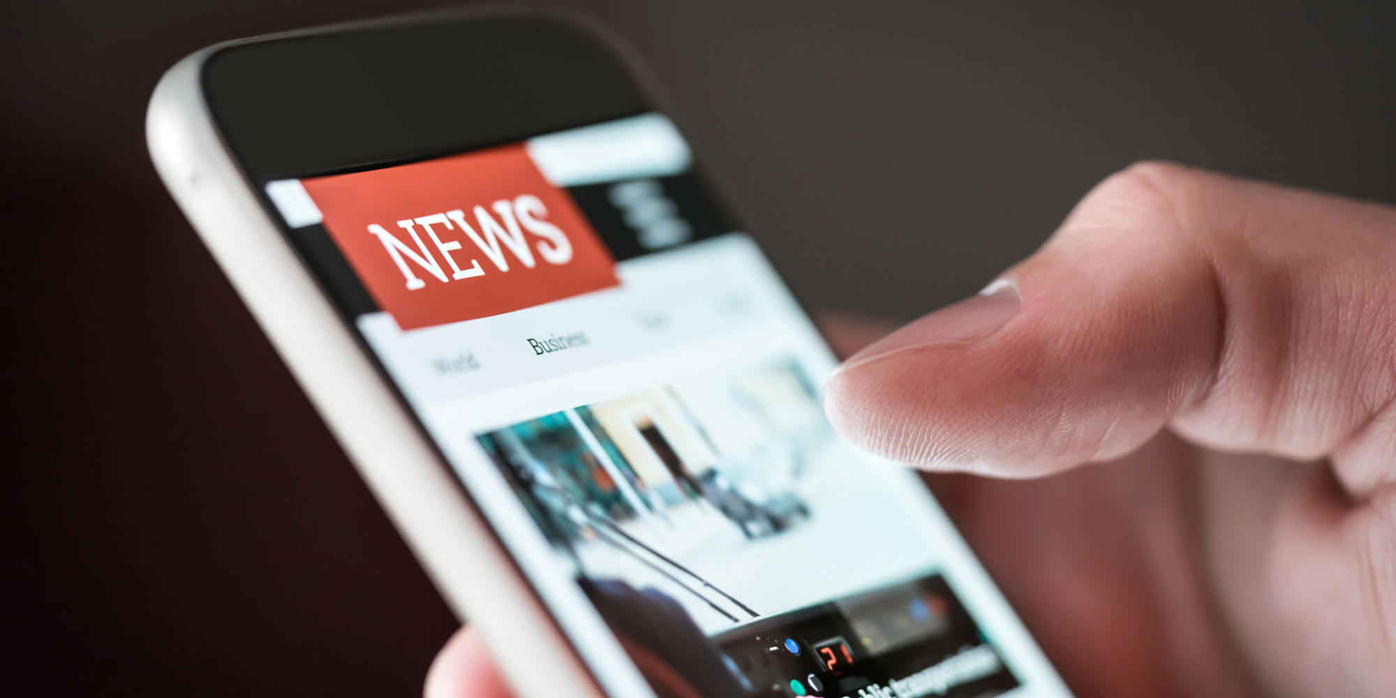 A person's hand is holding a smartphone displaying a news website with various news categories.