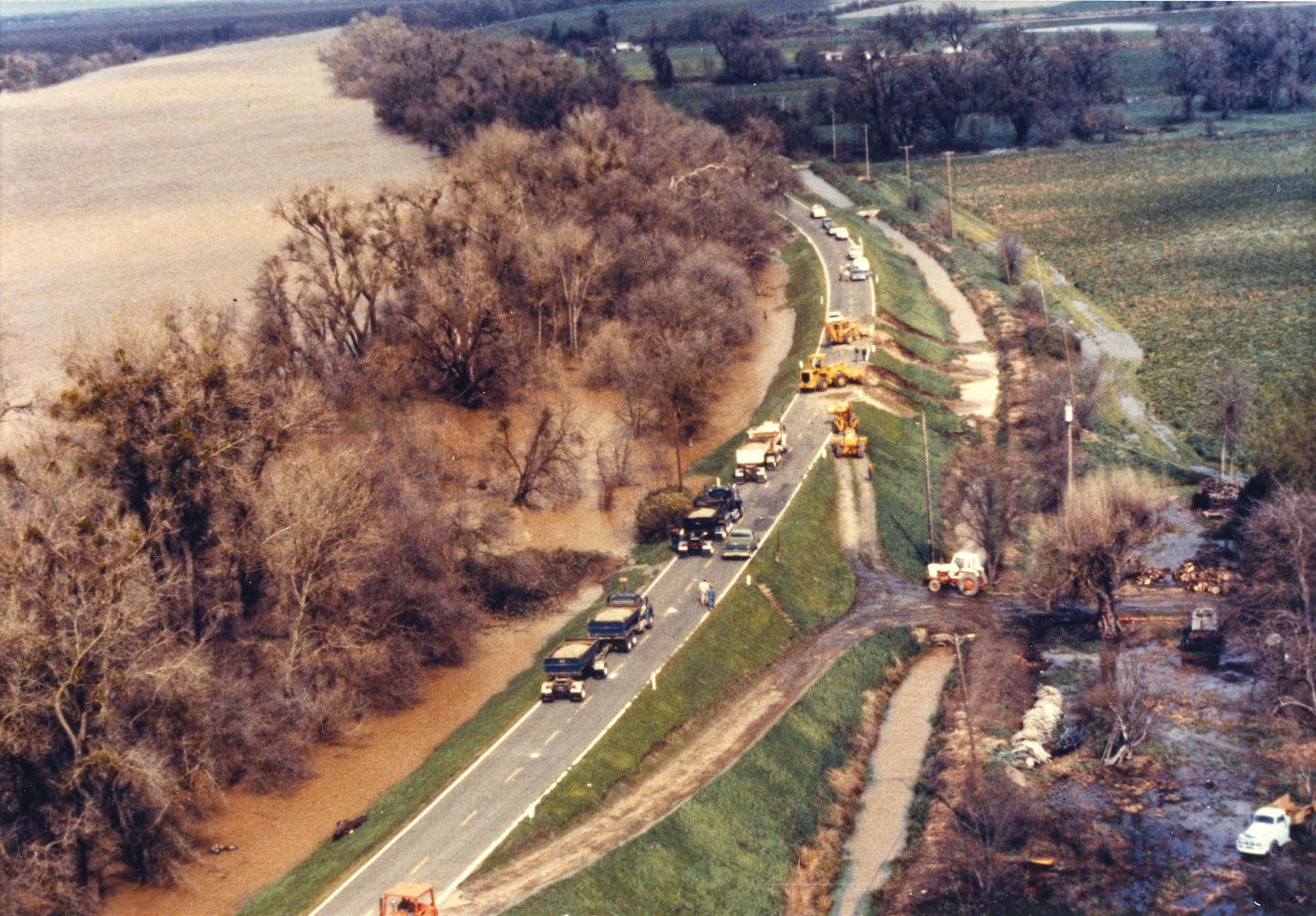 An aerial view of a flooded area next to a road, featuring vehicles and construction equipment working on the infrastructure.