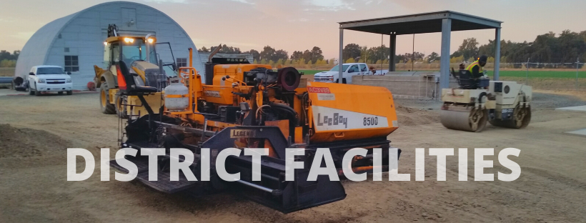 The image shows construction equipment, including a road paver and a roller, in a work area labeled "DISTRICT FACILITIES."
