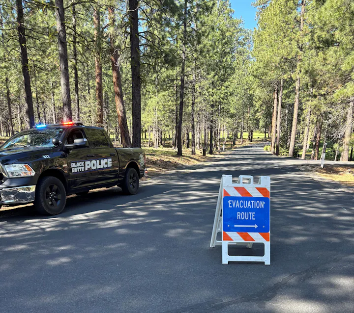 A police truck with flashing lights near a forest, alongside an "Evacuation Route" sign.