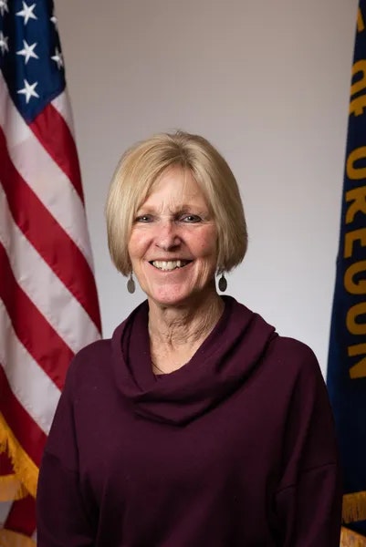 A woman smiling in front of American and Oregon flags.