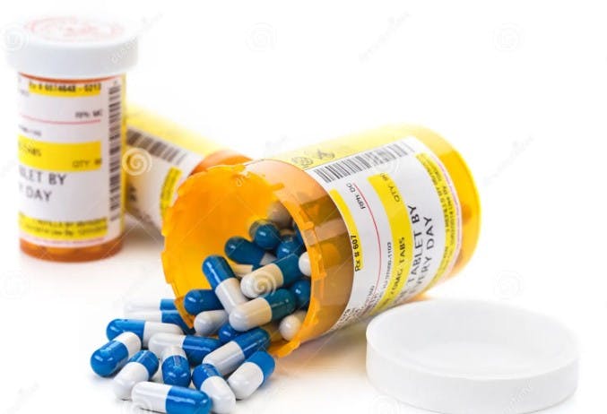 Prescription pill bottles with blue and white capsules spilled out.