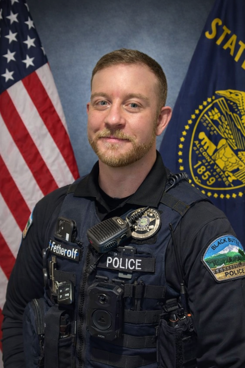 The image shows a police officer in uniform standing in front of an American flag, with police gear and badges on display.