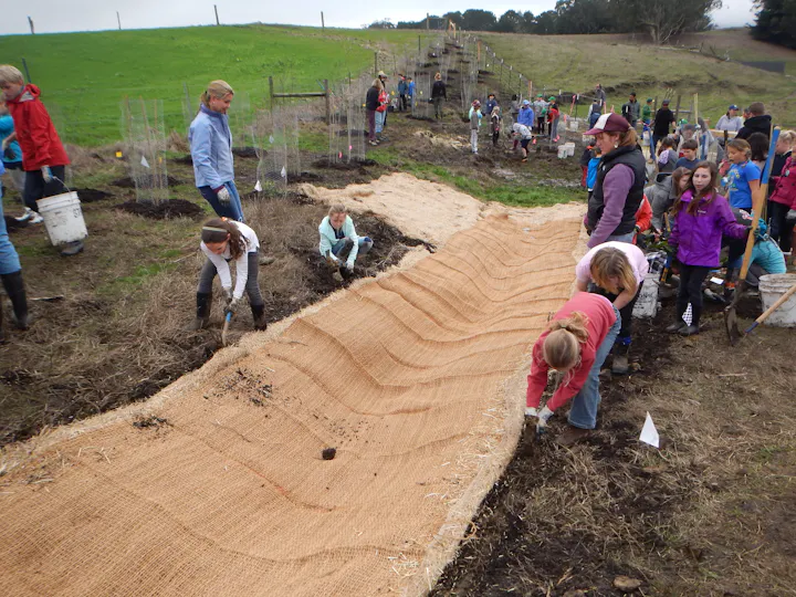 A group of children and adults is working together on a farm to plant and nurture crops.
