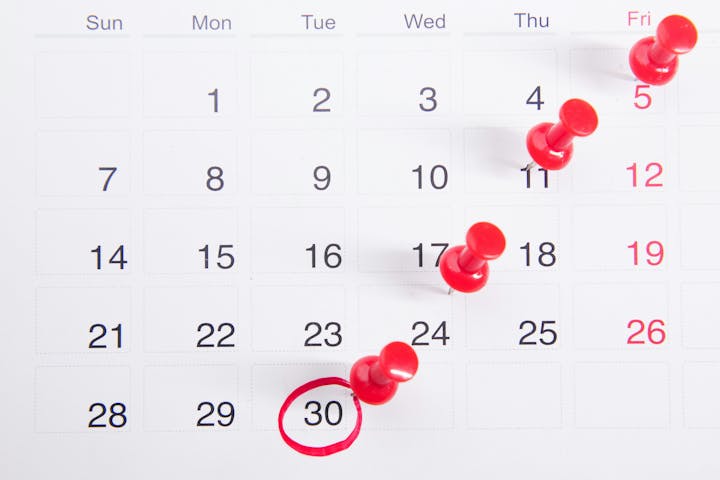 A calendar with red thumbtacks marking specific dates and a circle around the 30th.