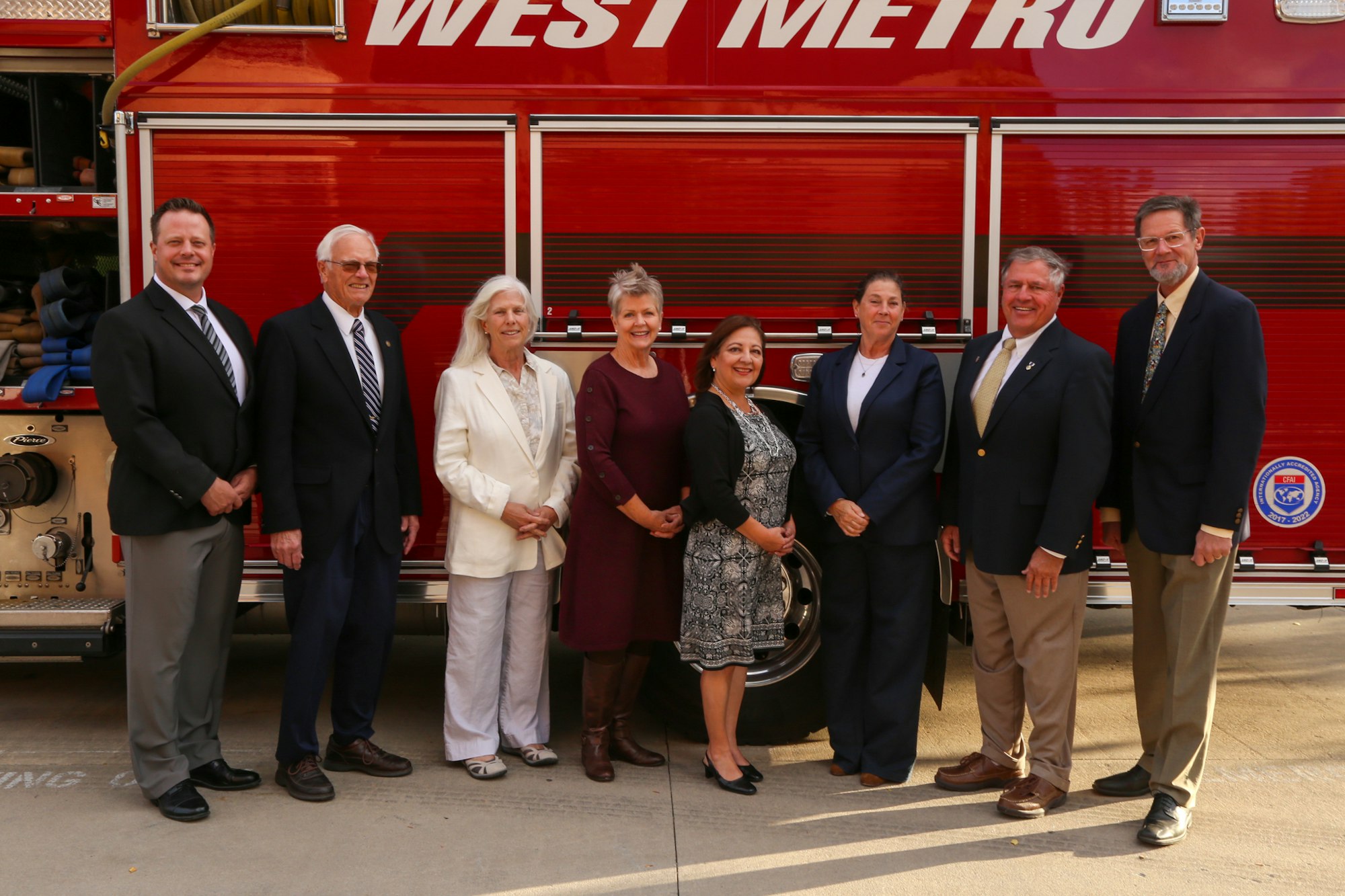 A group of seven adults posing in front of a red West Metro fire engine.