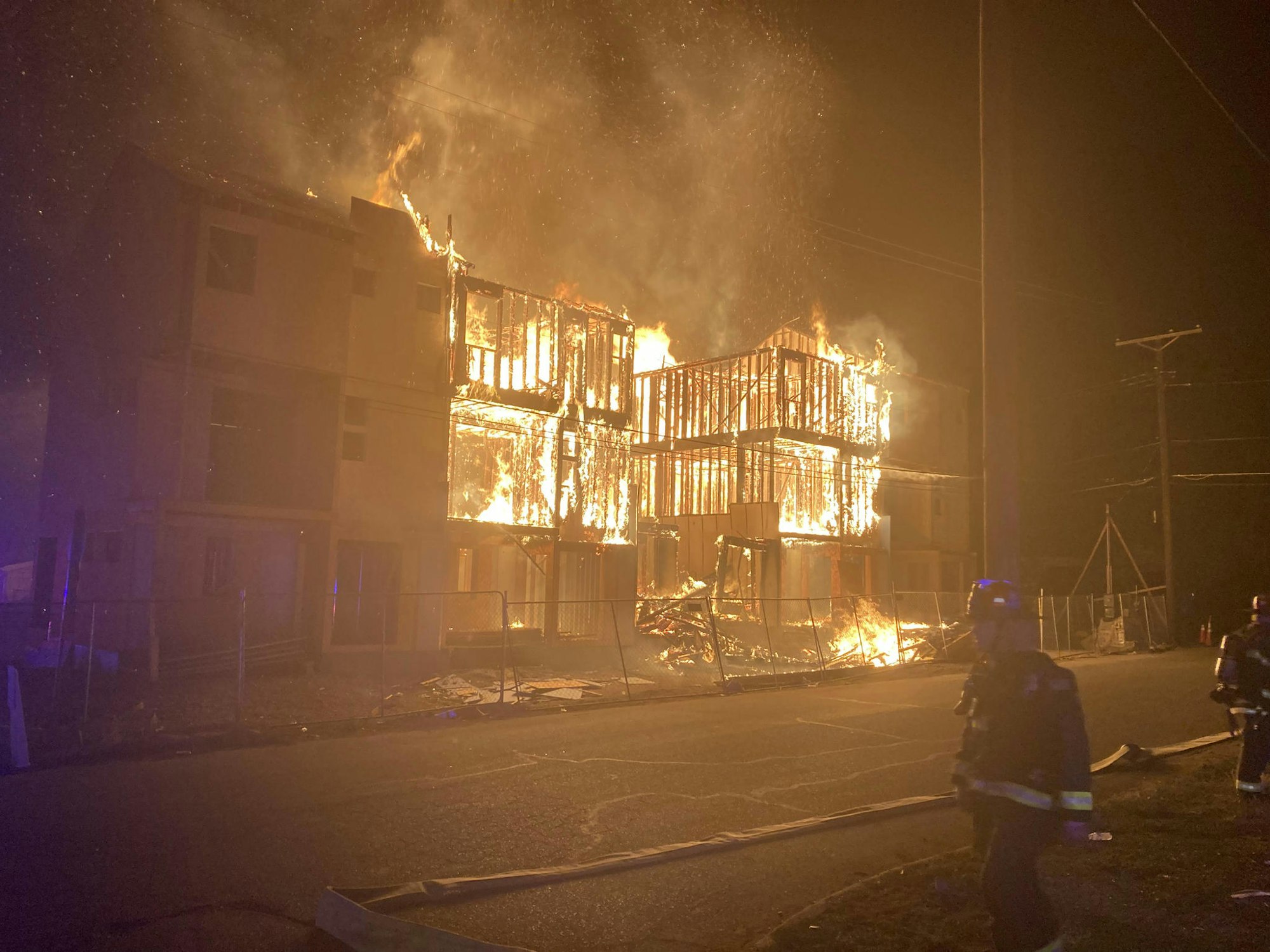 Fire at townhome construction site. Picture shows structure on fire with a firefighter in the foreground.