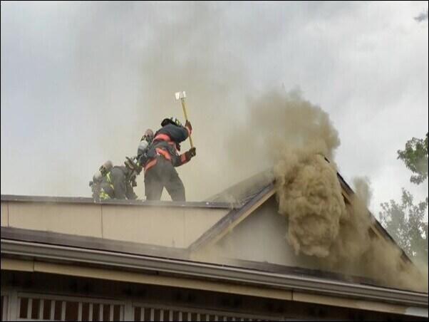 Firefighter swinging axe on top of roof during structure fire