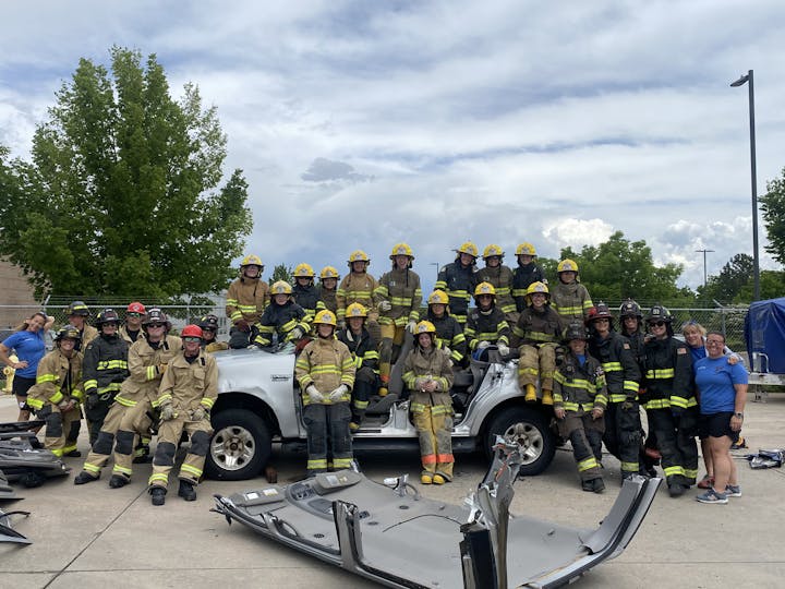Camp Ember participants & Instructors in firefighter gear posing with a dismantled vehicle during training.