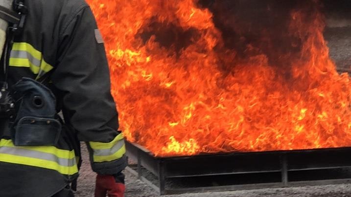 A firefighter in protective gear standing near a controlled fire.