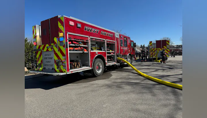 A red fire truck labeled "West Metro Fire Rescue" with firefighters and equipment, set against a clear blue sky.