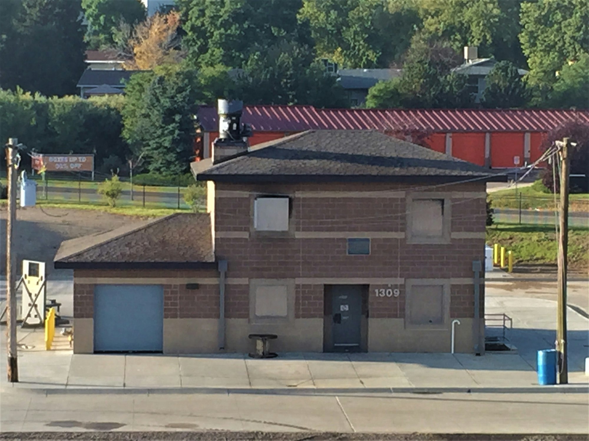 A small brick building with a garage door, a bench, and surrounding greenery.