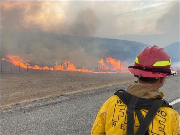 Firefighter in foreground, facing flames on the ground during the Oak Fire