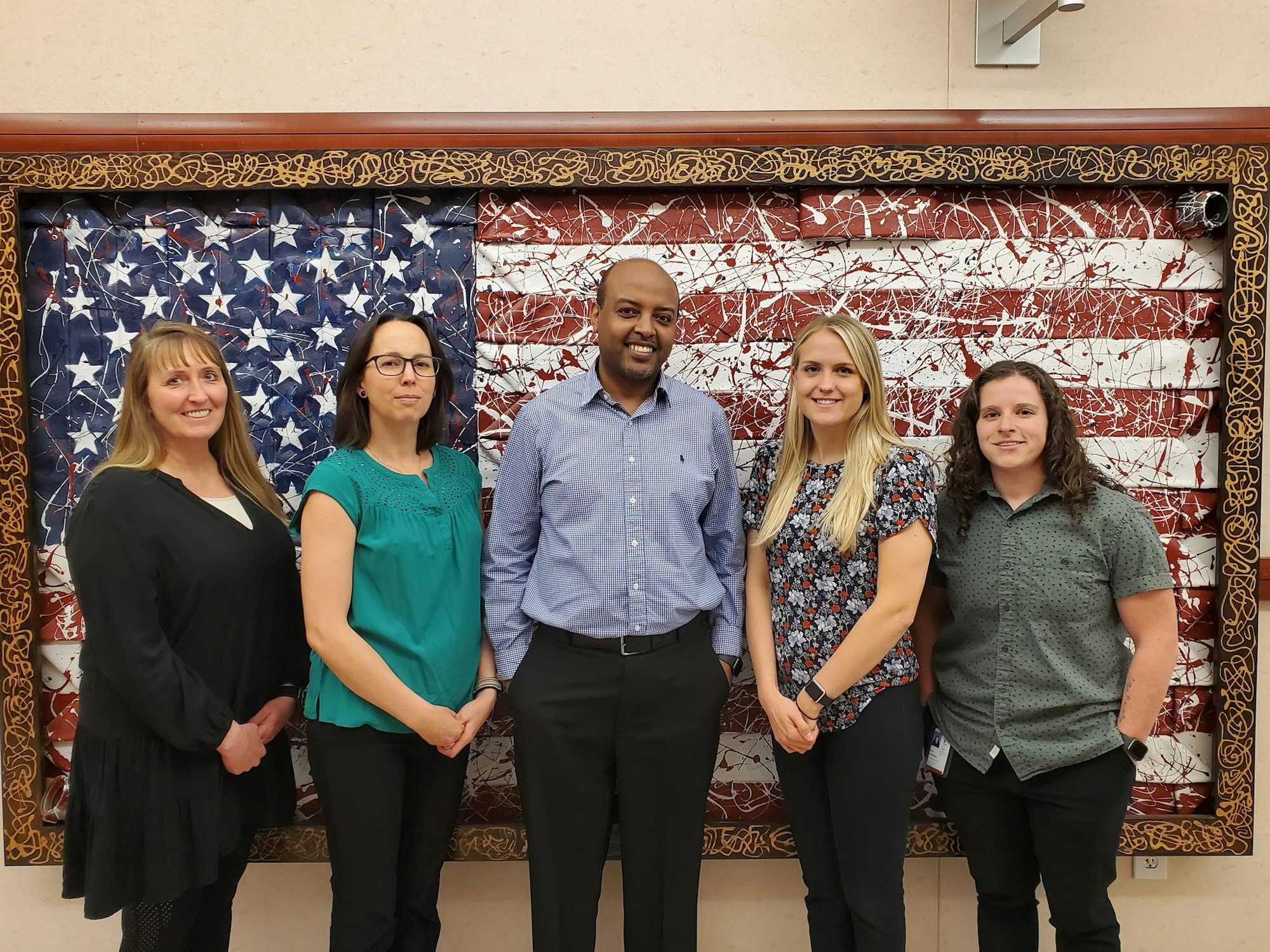 Group picture of West Metro's finance division, standing in front of an American flag, made out of retired fire hose.
