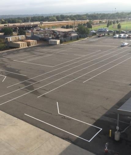 An empty parking lot with white-painted parking lines, a few vehicles in the distance, and a partly cloudy sky.
