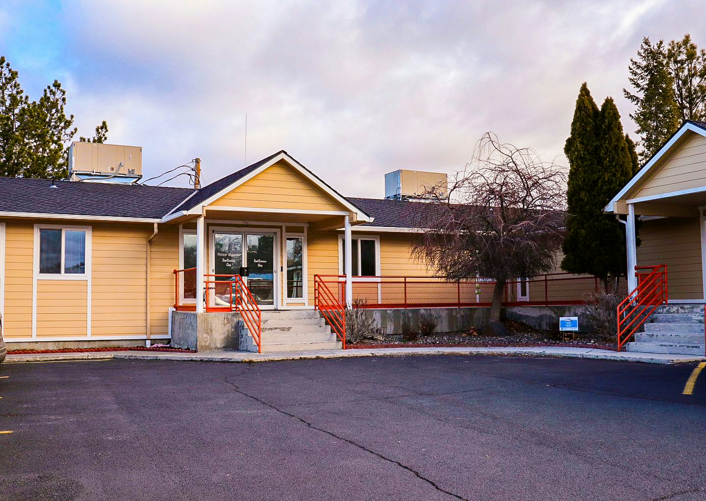 A single-story beige building with red railings and overcast skies.