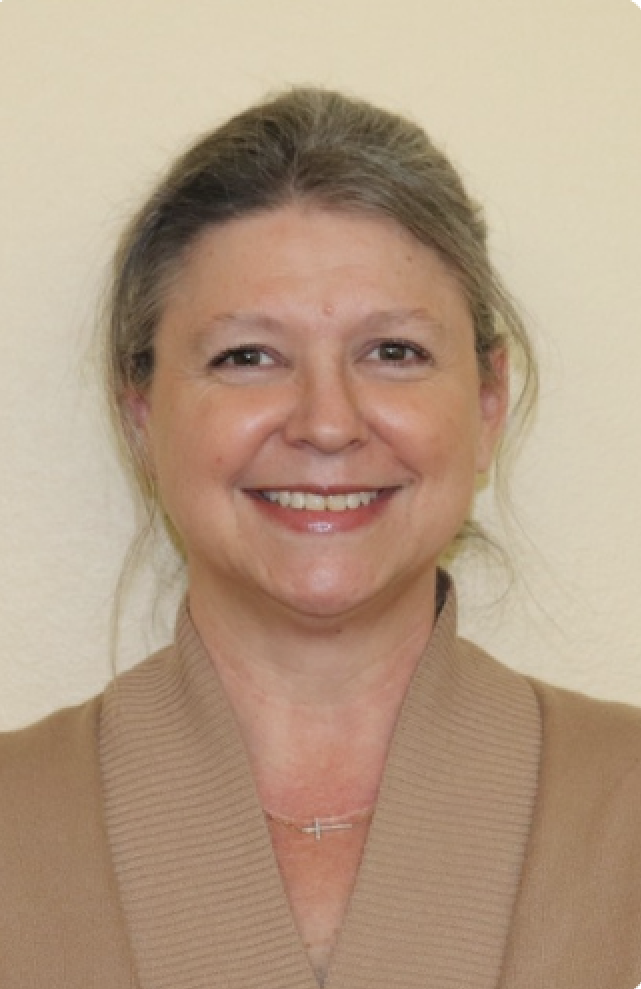 A smiling woman with a cross necklace and a beige top.