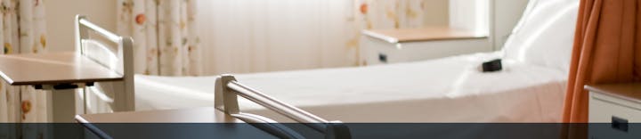 A bright hospital room featuring a bed, bedside tables, and curtains with floral patterns.