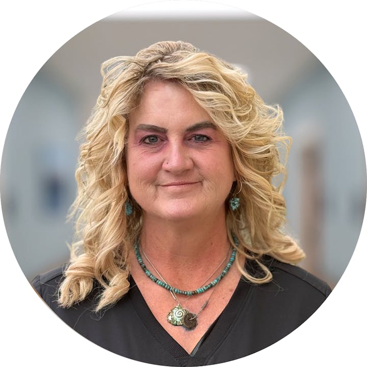 A person with curly blonde hair and wearing turquoise jewelry, smiling at the camera.