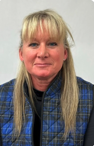 A person with long blonde hair, wearing a blue plaid vest over a black top, posing for a photo.