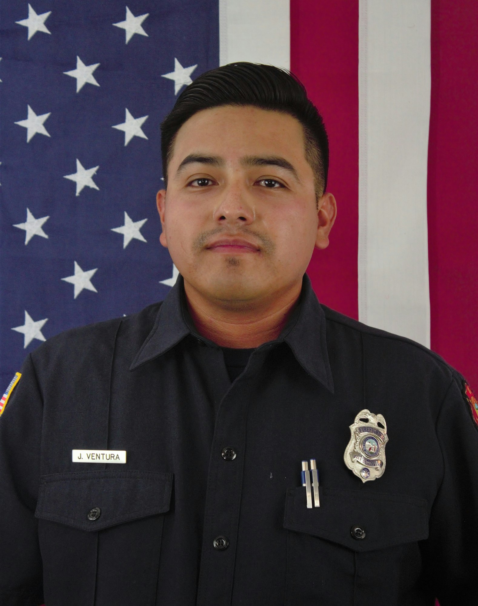 The image features a man in a dark uniform with a name tag "J. Ventura," standing in front of an American flag backdrop.