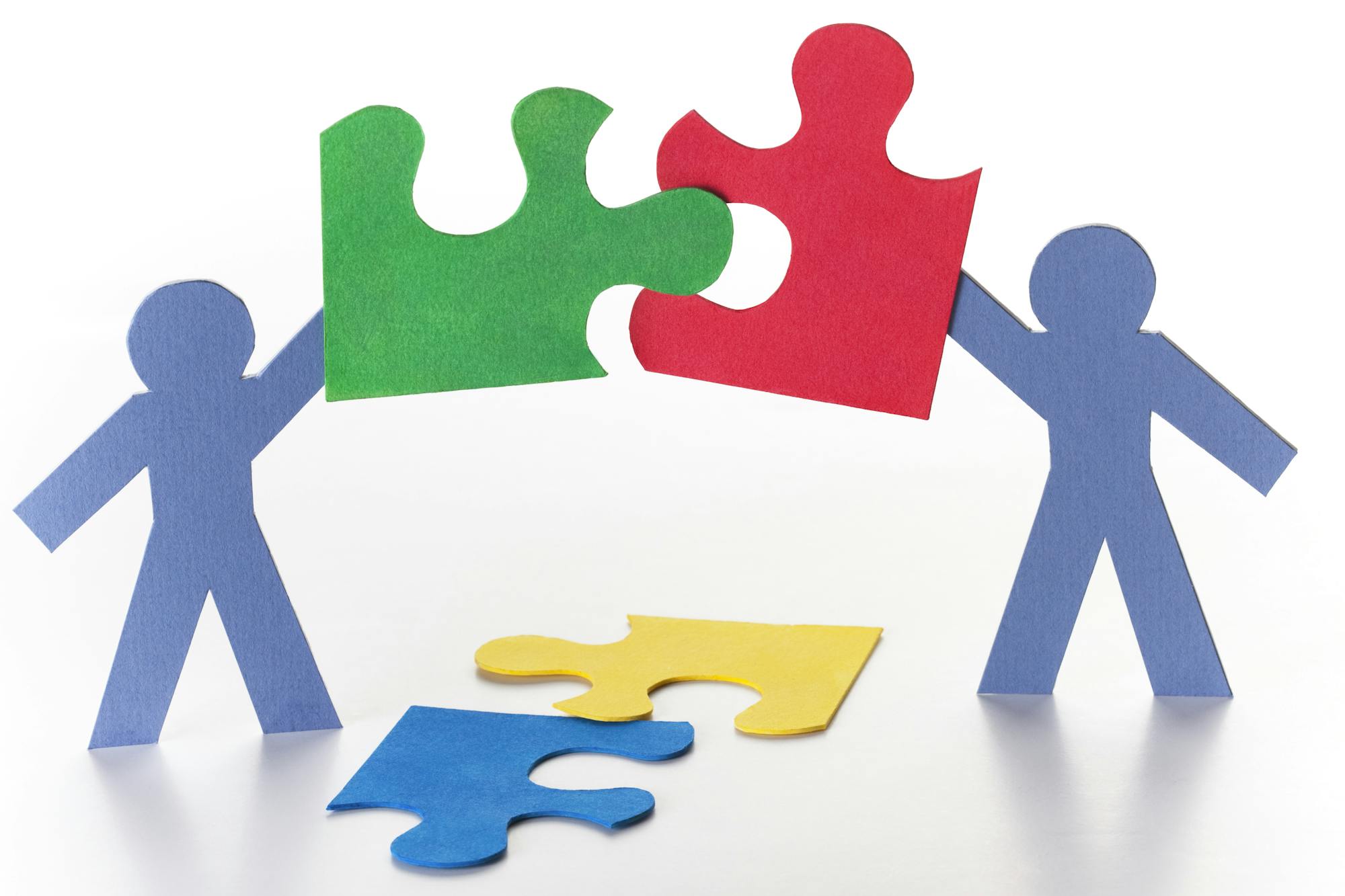 Paper cutouts of people holding connecting puzzle pieces.