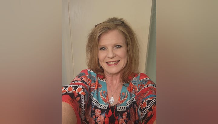 A smiling woman wearing a colorful top and a silver necklace.
