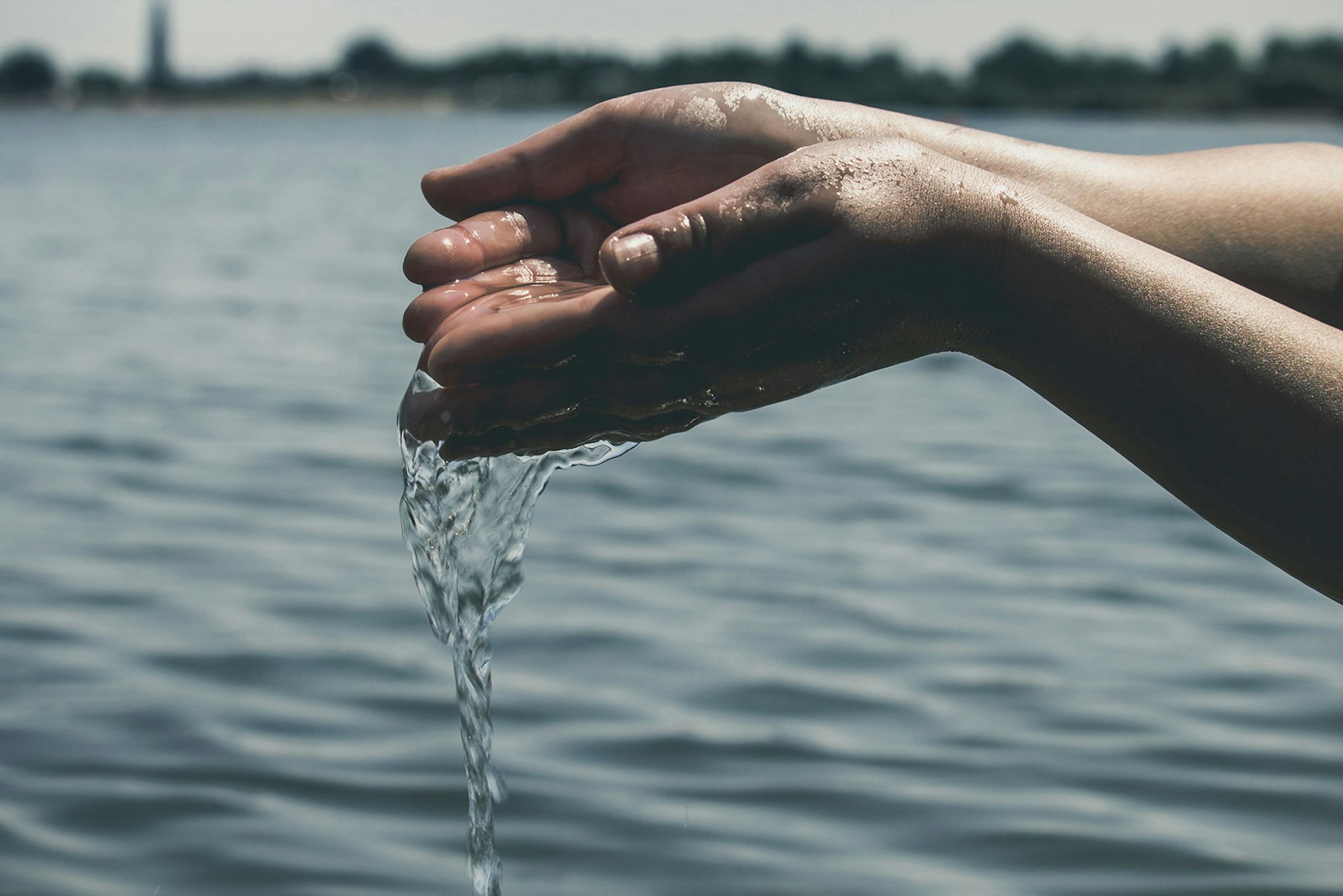 Hands cupping water above a body of water, with droplets flowing down.