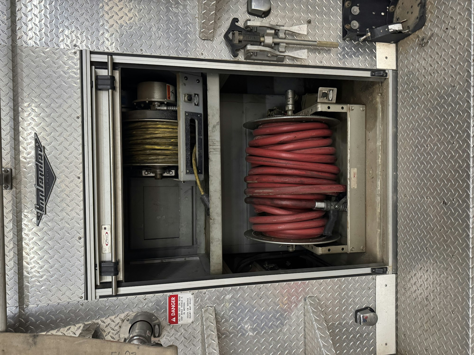 Coiled hoses stored in a compartment of a vehicle with diamond plate metal and warning labels.