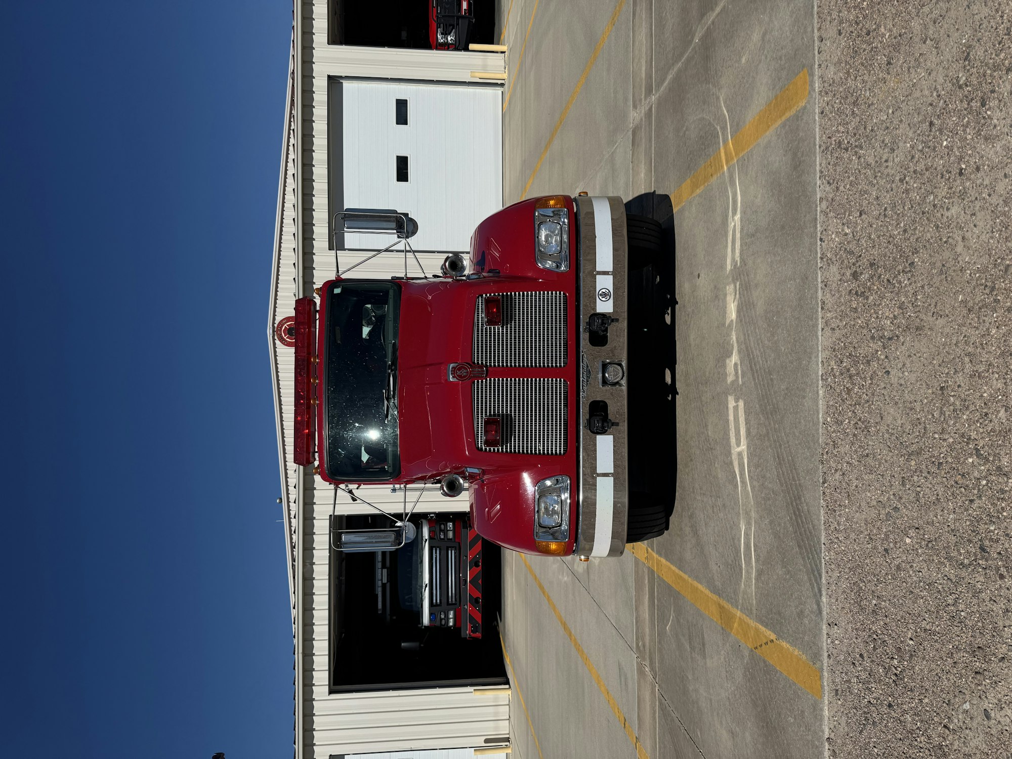 A red fire truck parked in front of a fire station with a blue sky above.