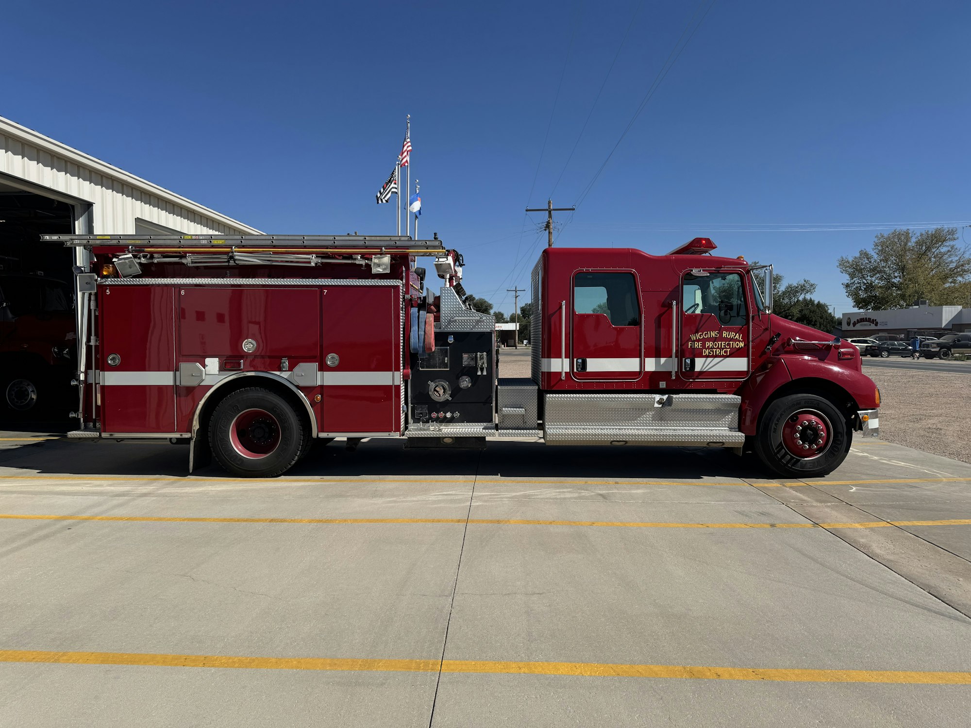 A red fire truck parked outside a garage with "Wiggins Rural Fire Protection District" on the side.