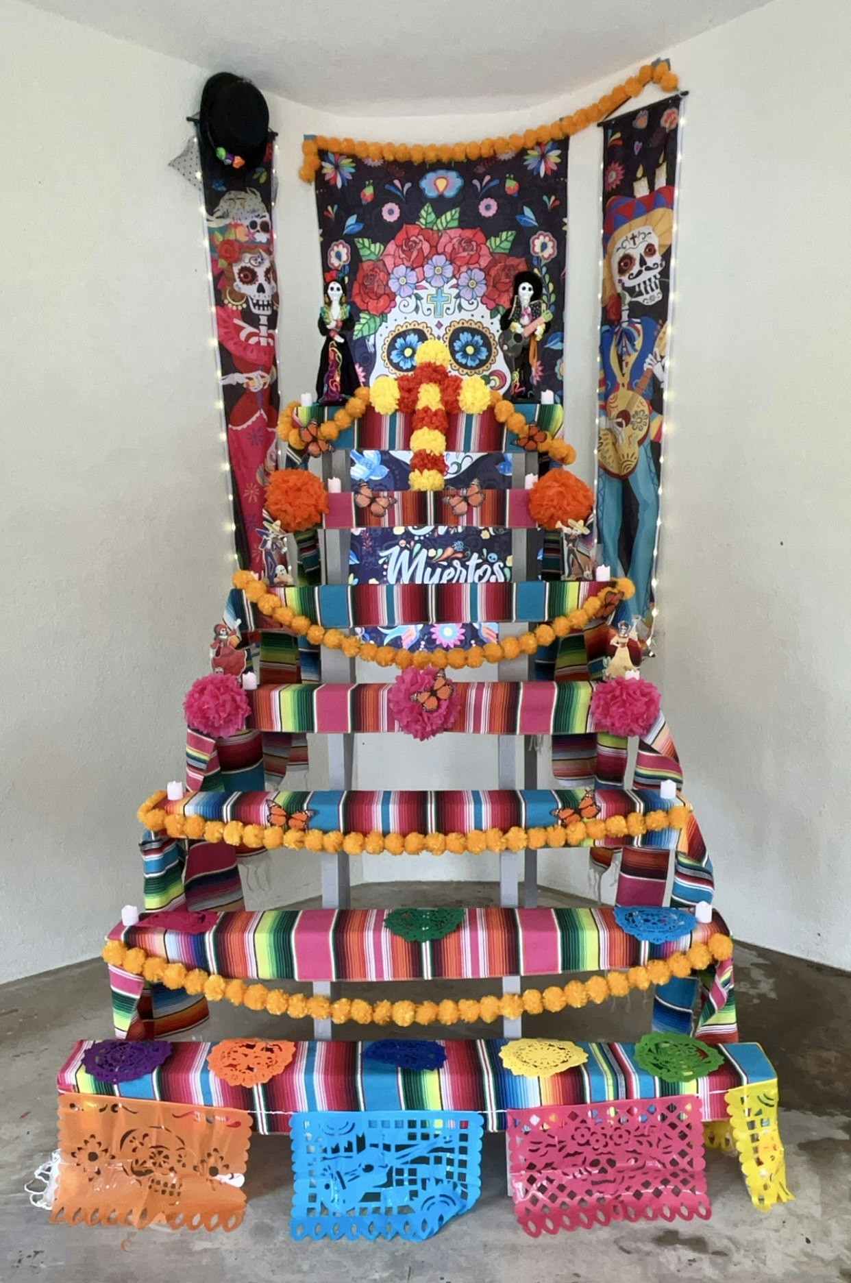 A colorful Day of the Dead altar with skull imagery, vibrant textiles, marigolds, and paper decorations.