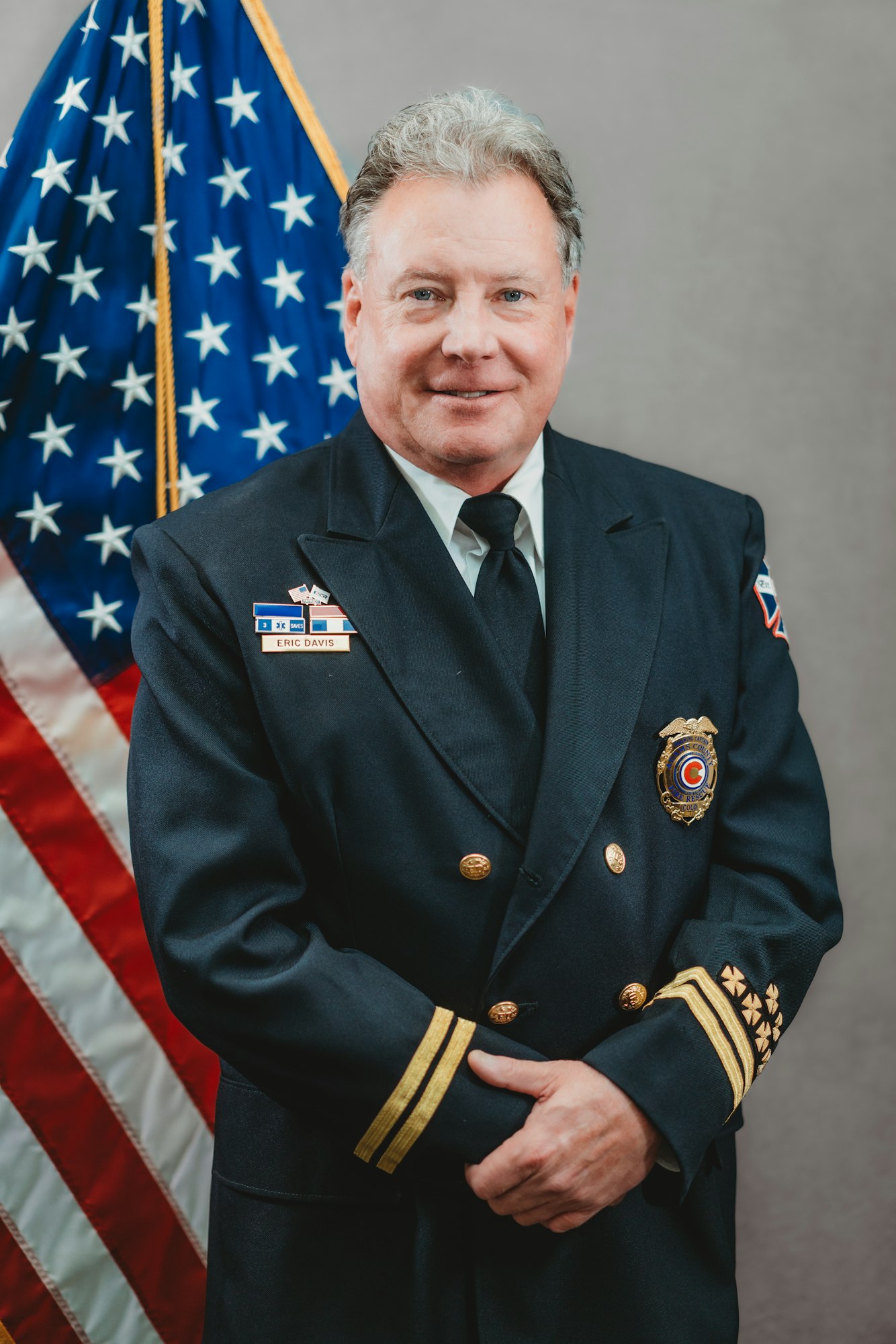 A person in a formal uniform stands in front of an American flag.