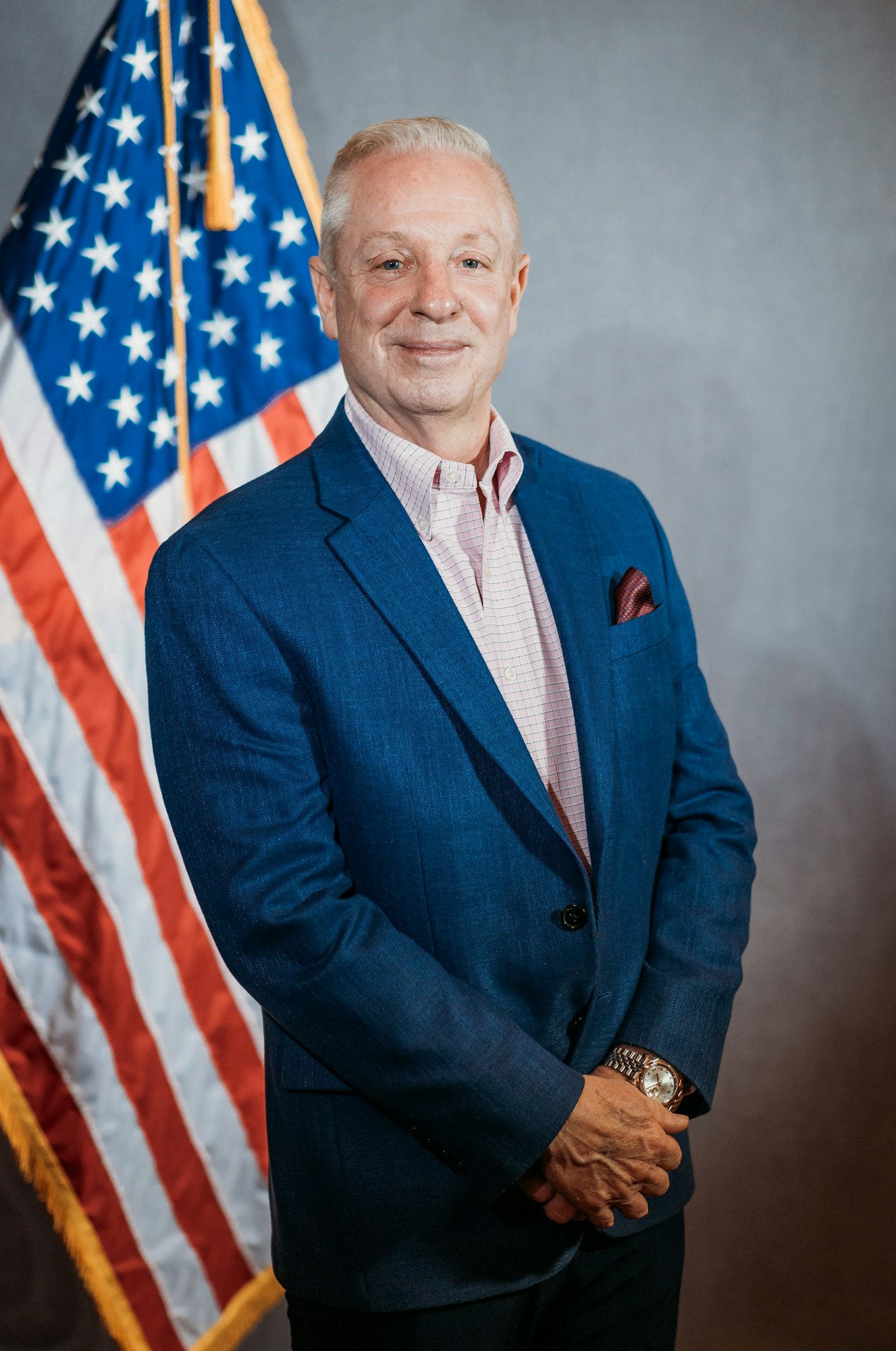 A person in a blue suit stands in front of a U.S. flag.