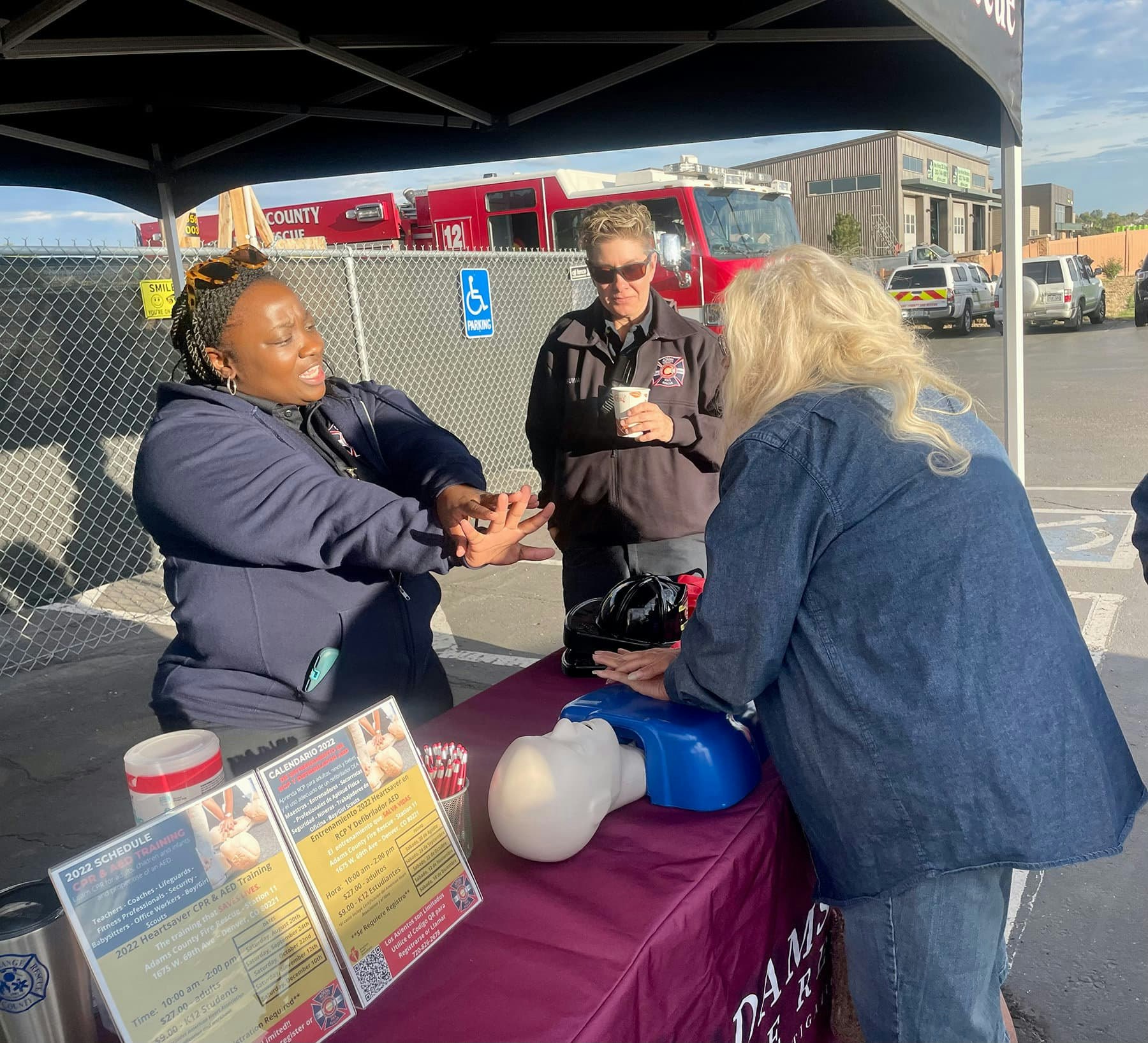People at a table practicing CPR with a mannequin, near a fire truck.