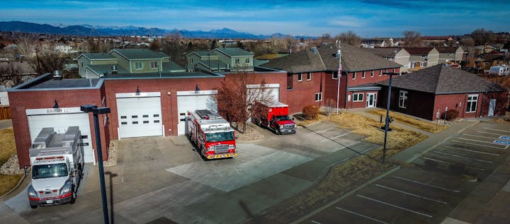 Fire station with red engines, trucks, and parking lot; mountains in the background.