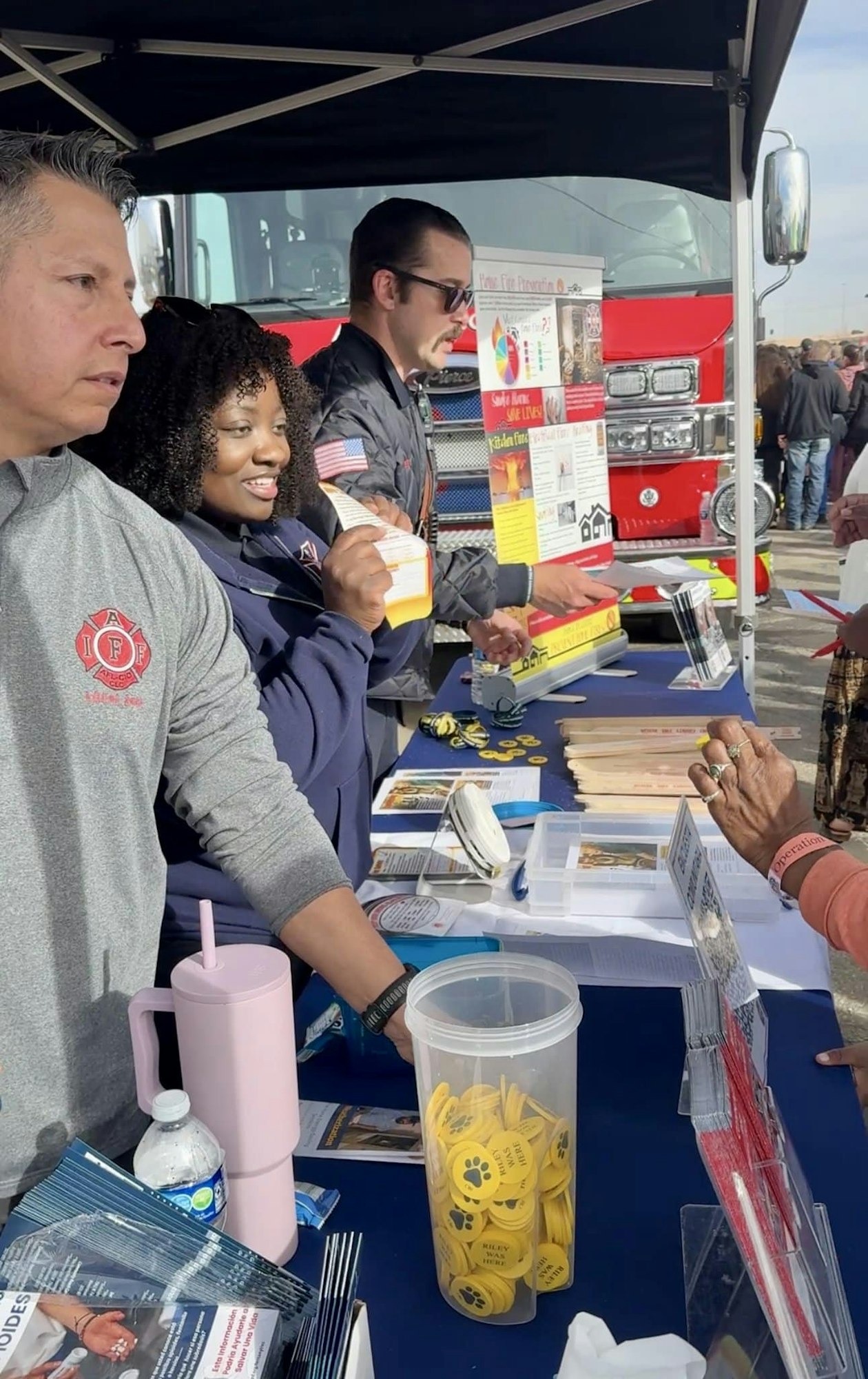 A group of people at an outdoor booth with pamphlets and items, near a red fire truck.